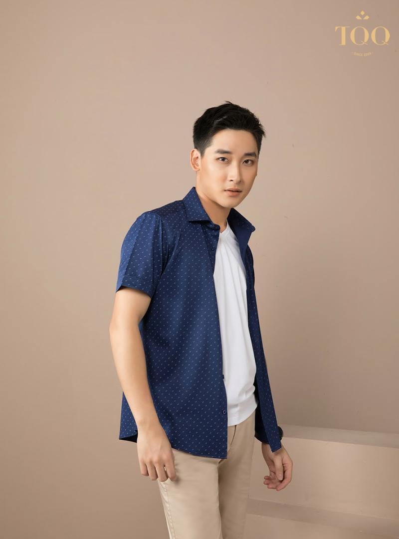 Một người đàn ông trẻ với phong cách thời trang đường phố, mặc áo sơ mi kẻ sọc flannel được khoác ngoài một chiếc áo thun trắng, quần jeans rách gối và đi giày sneakers. Anh ấy đang tự tin bước đi trên đường phố đô thị.